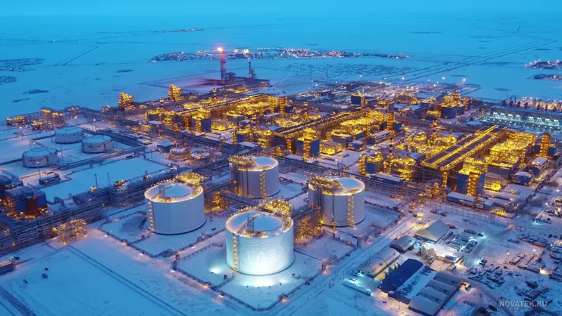 Aerial view of an industrial facility in a snowy landscape, illuminated by numerous lights, featuring large storage tanks and refinery structures.